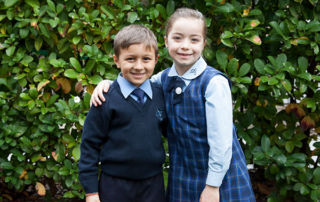 Two students at St Michael's Catholic Primary School Daceyville smiling in front of green hedge
